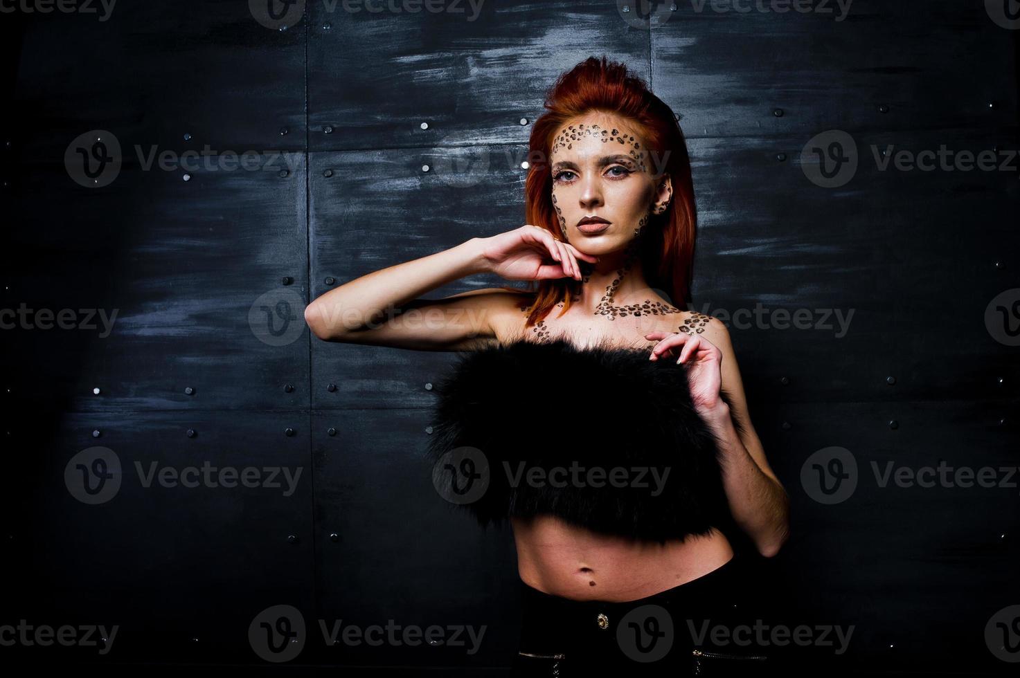 Fashion model red haired girl with originally make up like leopard predator against steel wall. Studio portrait. photo