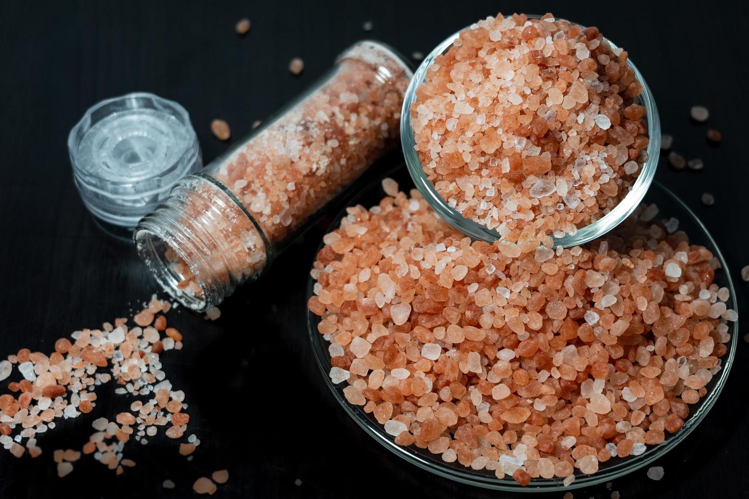 Himalayan salt is in clear jar and on plate placed on black wooden table photo