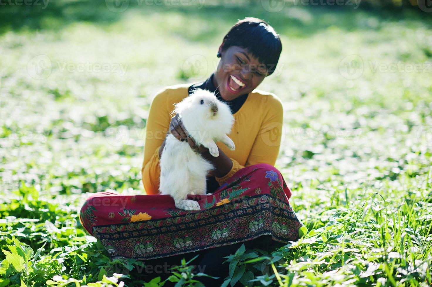 African american girl at yellow and red dress with white rabbit at hands. photo