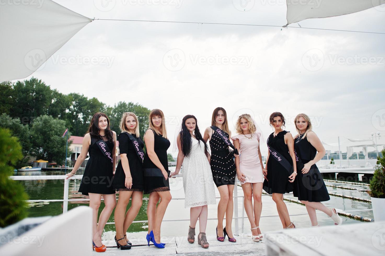 Group of 8 girls wear on black and 2 brides at hen party having fun at pier on beach side. photo