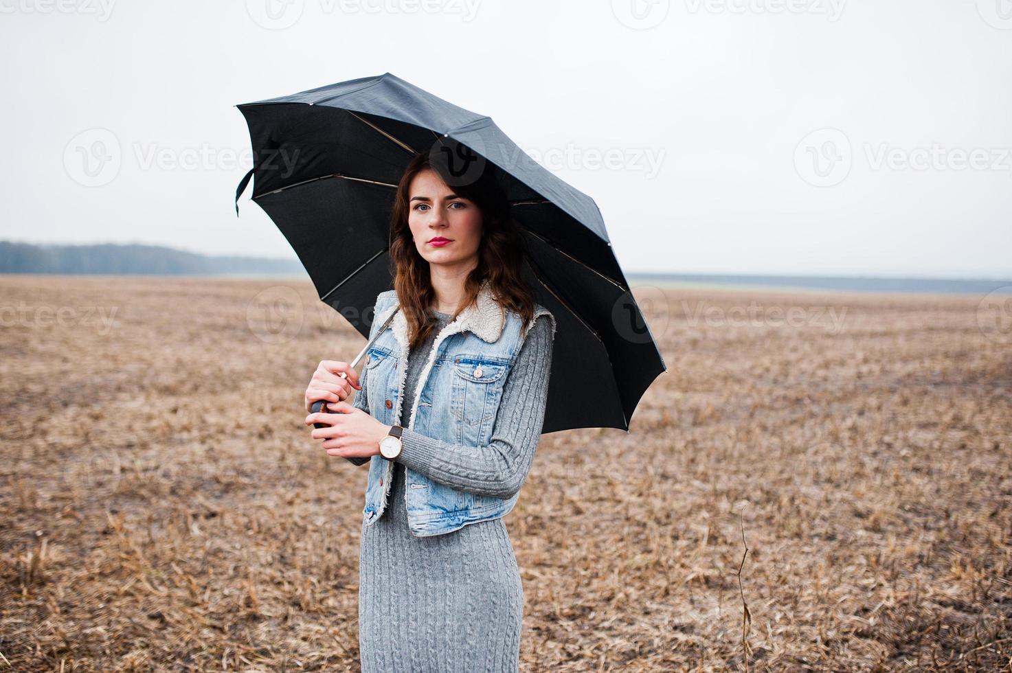 Portrait of brunette curly girl in jeans jacket with black umbrella at field. photo