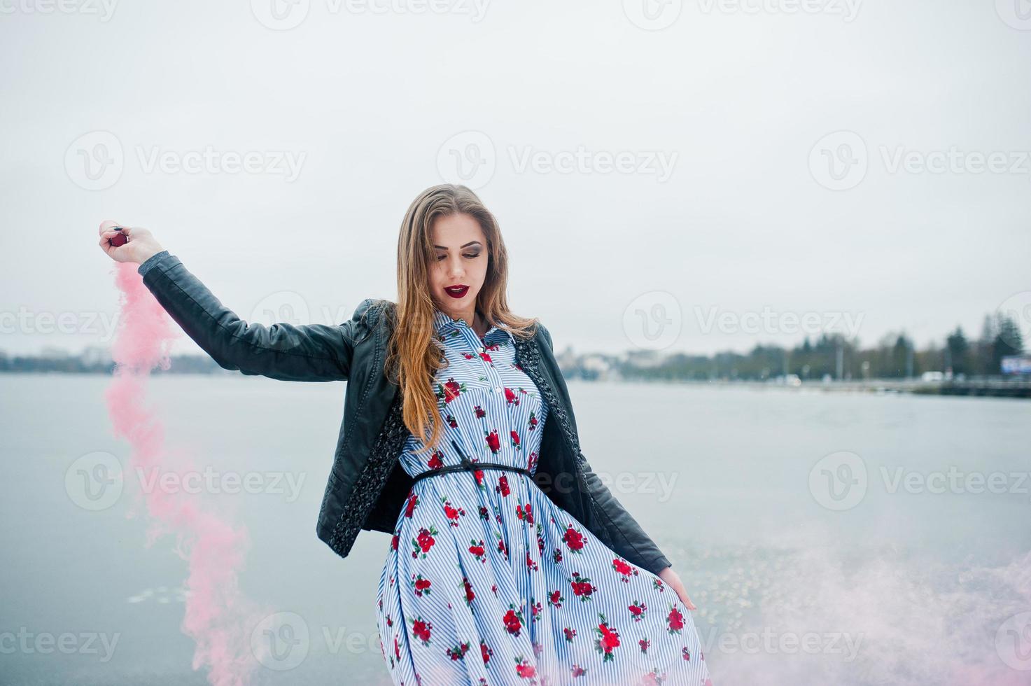 Stylish girl in leather jacket hold pink smoke flare at winter day against frozen lake. photo