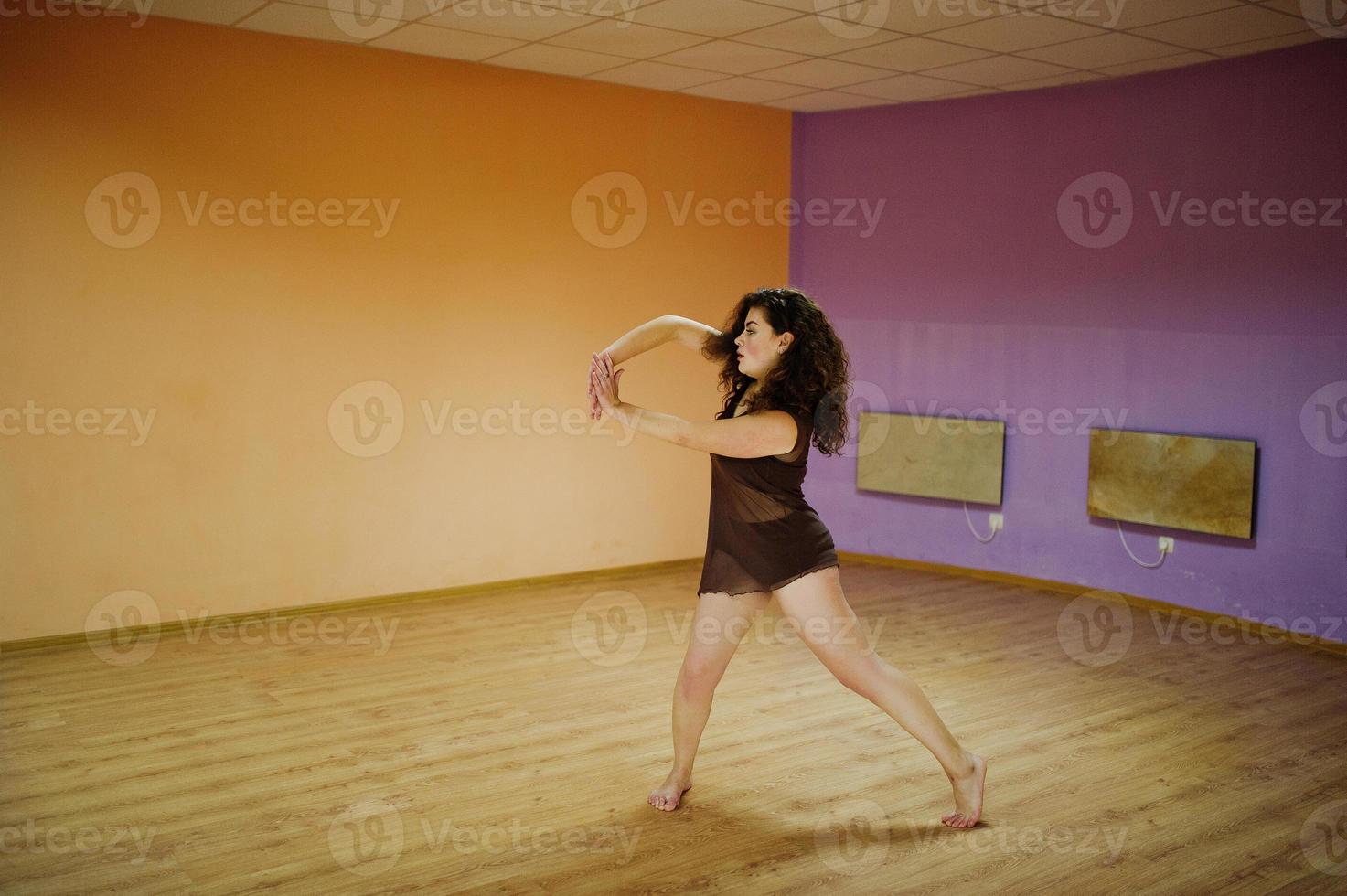 modelo morena rizada de talla grande haciendo acrobacias en la sala de baile. foto