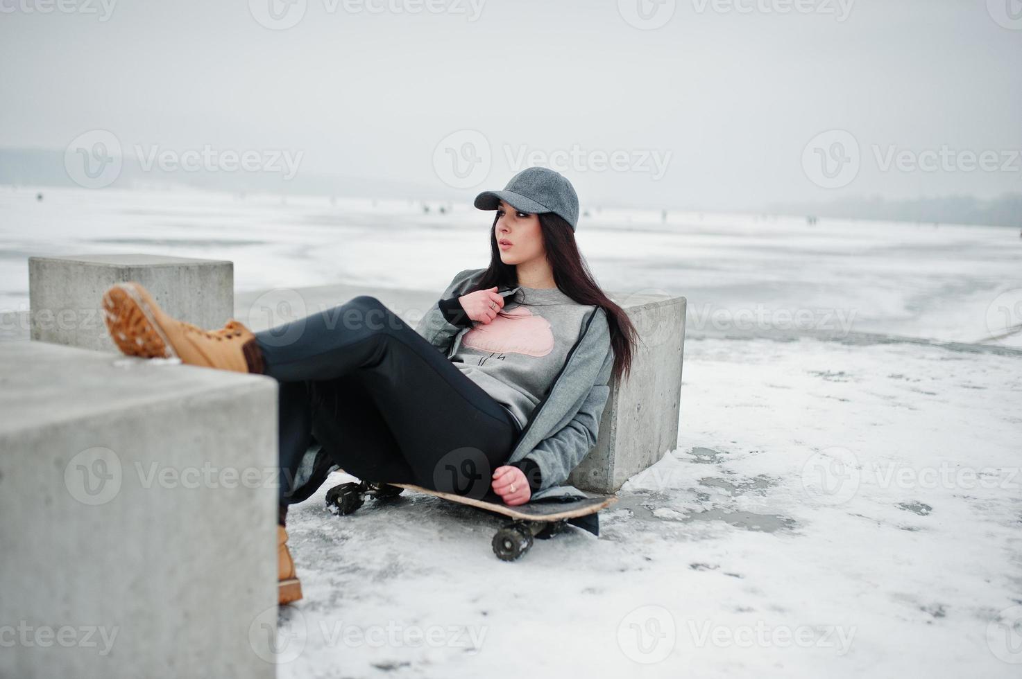 Stylish brunette girl in gray cap, casual street style with skate board on winter day. photo