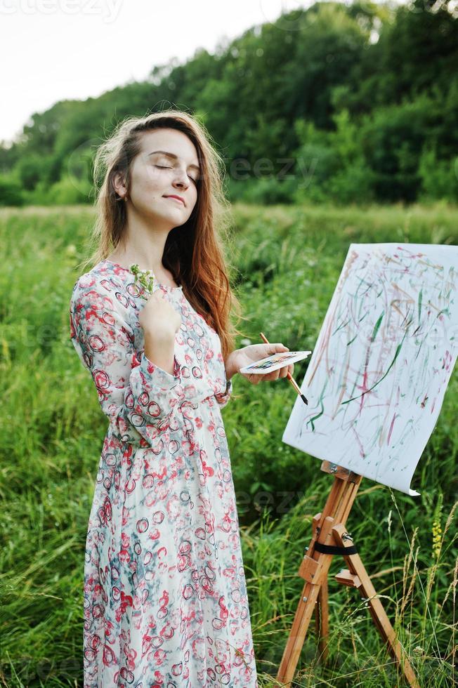 Portrait of an attractive young woman in long dress painting with watercolor in nature. photo