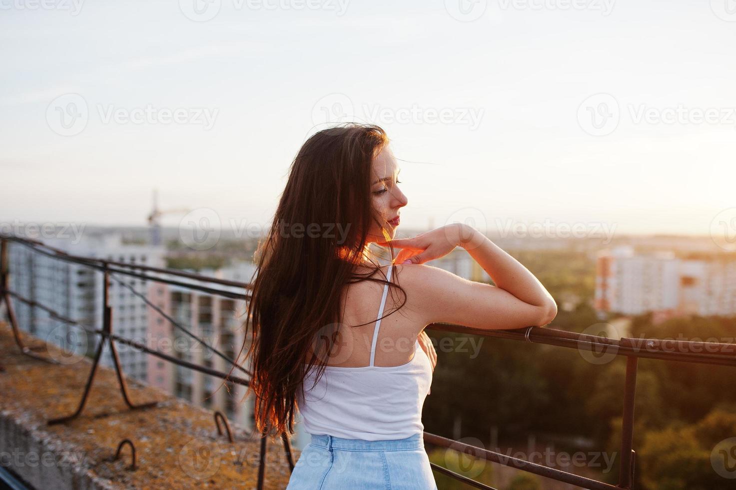 Portrait of a gorgeous young woman in casual clothing admiring the sunset from the roof of a building. photo