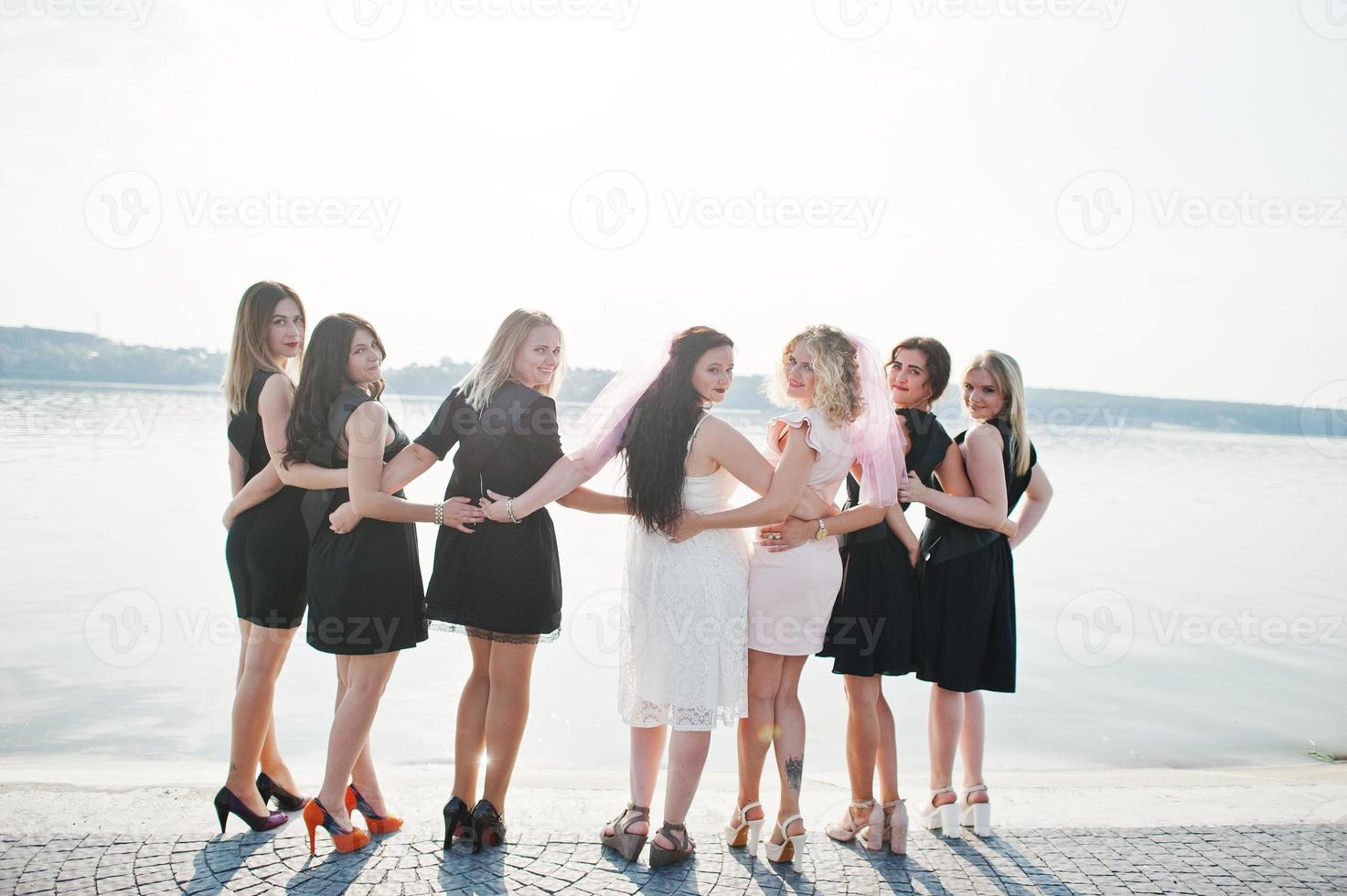 Back of group of 7 girls wear on black and 2 brides at hen party. photo