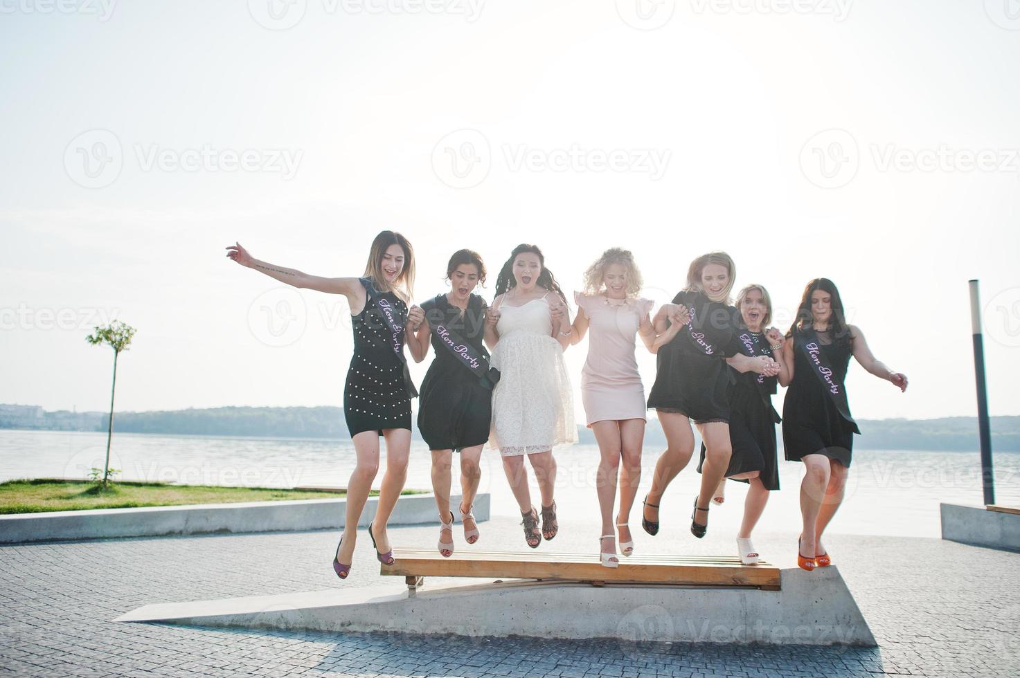 grupo de 7 chicas vestidas de negro y 2 novias saltando en la despedida de soltera. foto