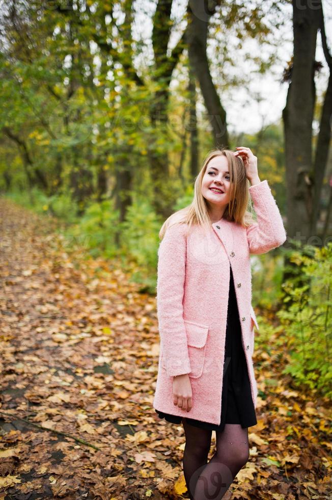 Young blonde girl at pink coat posed on autumn park. photo