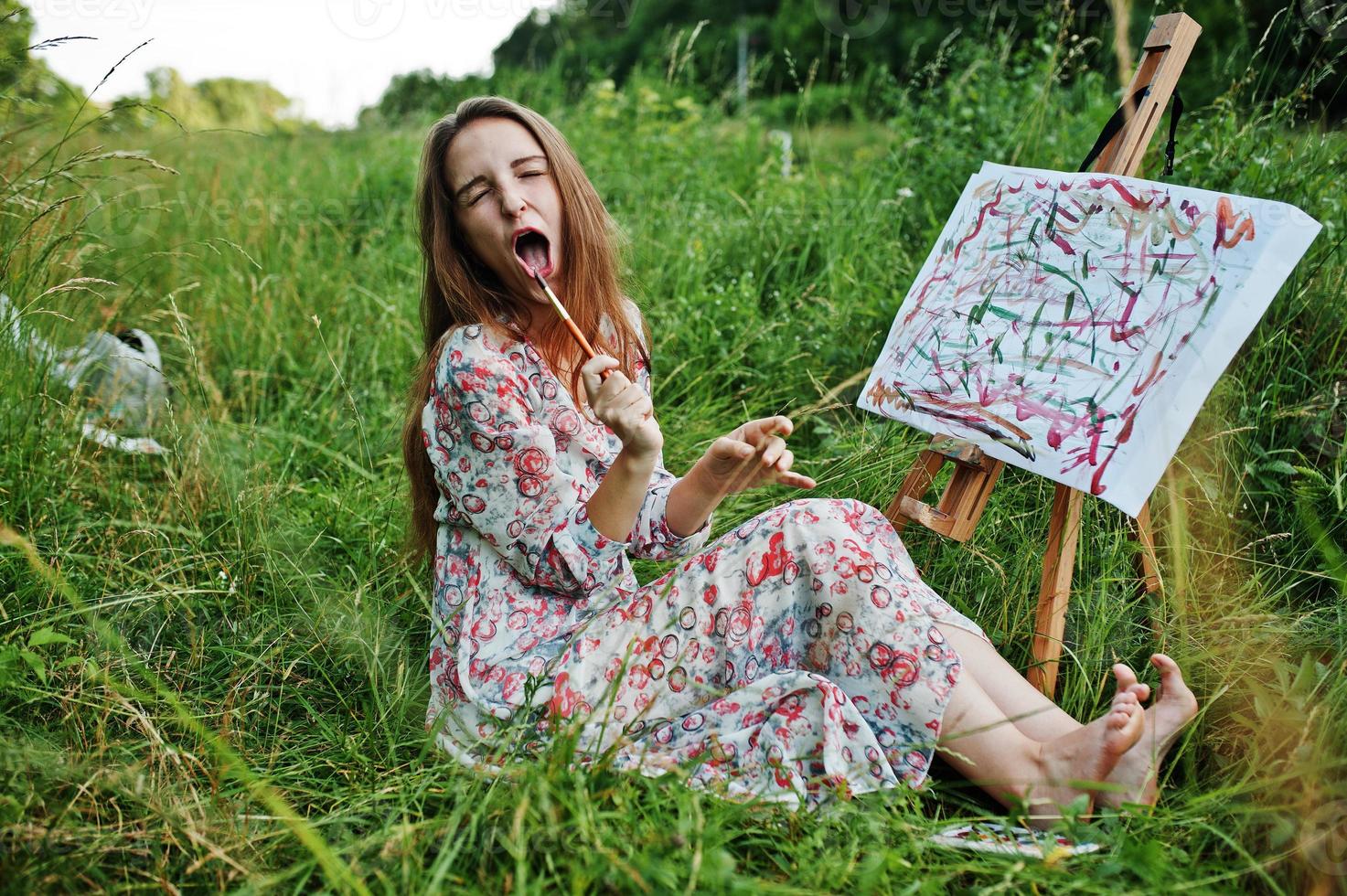 retrato de una chica divertida haciendo extrañas expresiones faciales mientras pinta en el prado. foto