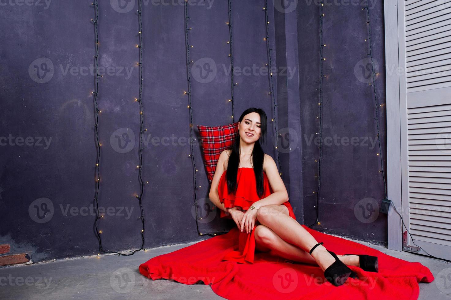 chica morena con vestido rojo posó cerca de la decoración de año nuevo en la sala de estudio. foto