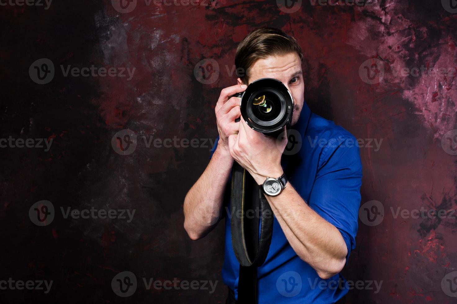 retrato de estudio de un elegante fotógrafo profesional con cámara, vestido con camisa azul y corbata. foto