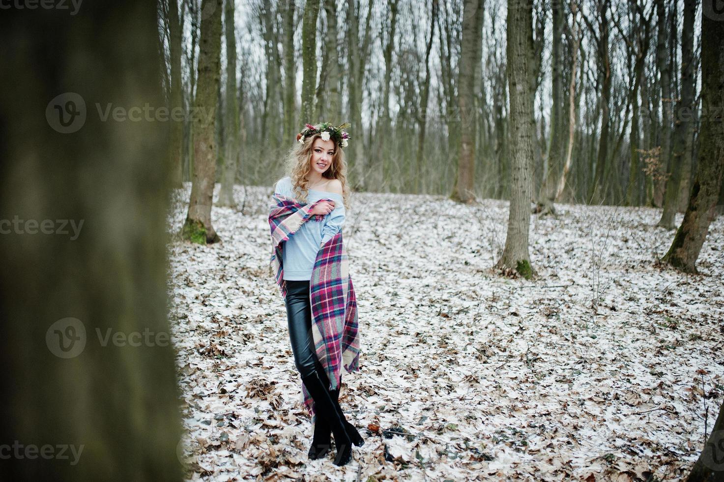 Curly cute blonde girl with wreath in checkered plaid at snowy forest in winter day. photo