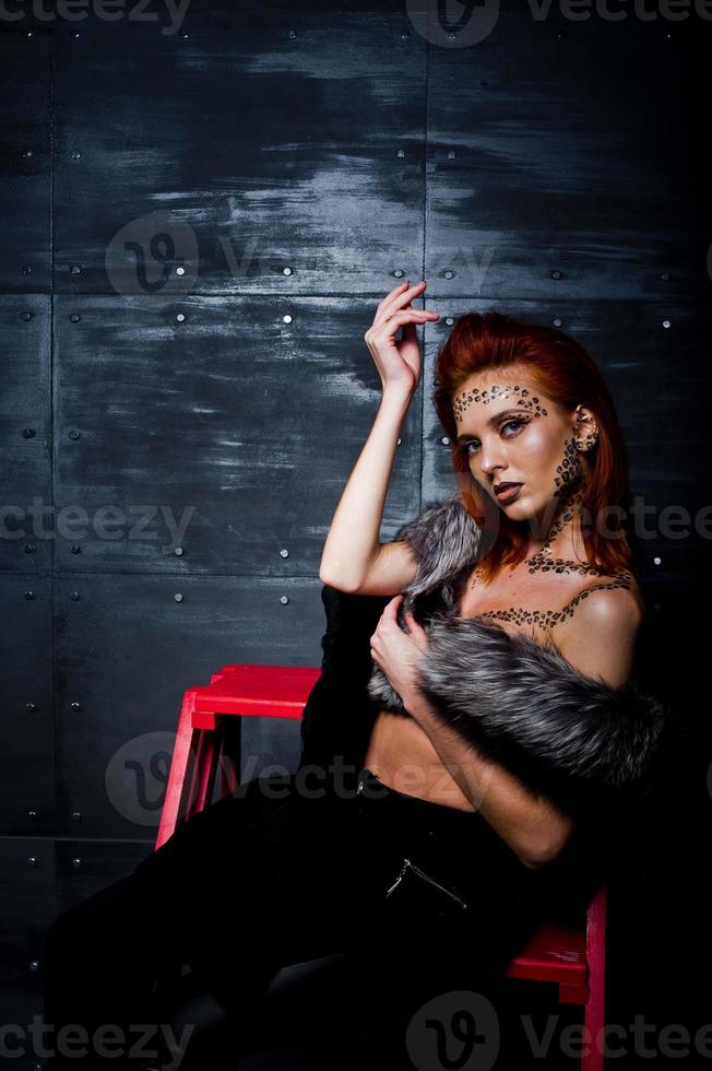 modelo de moda chica pelirroja con maquillaje original como depredador leopardo contra la pared de acero. retrato de estudio en la escalera. foto