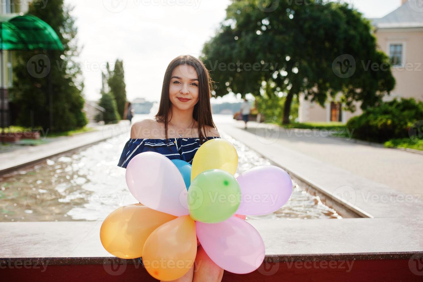 hermosa chica morena en la calle de la ciudad con globos en las manos. foto