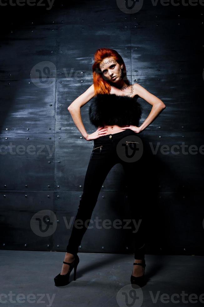 Fashion model red haired girl with originally make up like leopard predator against steel wall. Studio portrait. photo