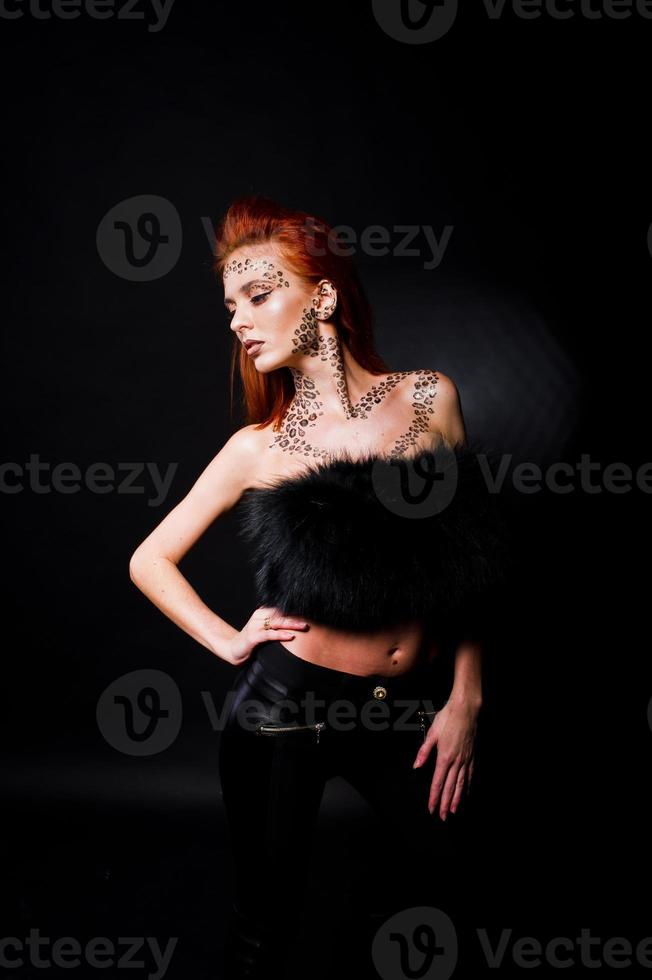 Fashion model red haired girl with originally make up like leopard predator isolated on black. Studio portrait. photo