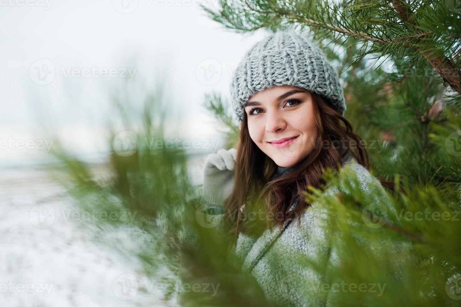 Portrait of gentle girl in gray coat and hat against new year tree outdoor. photo