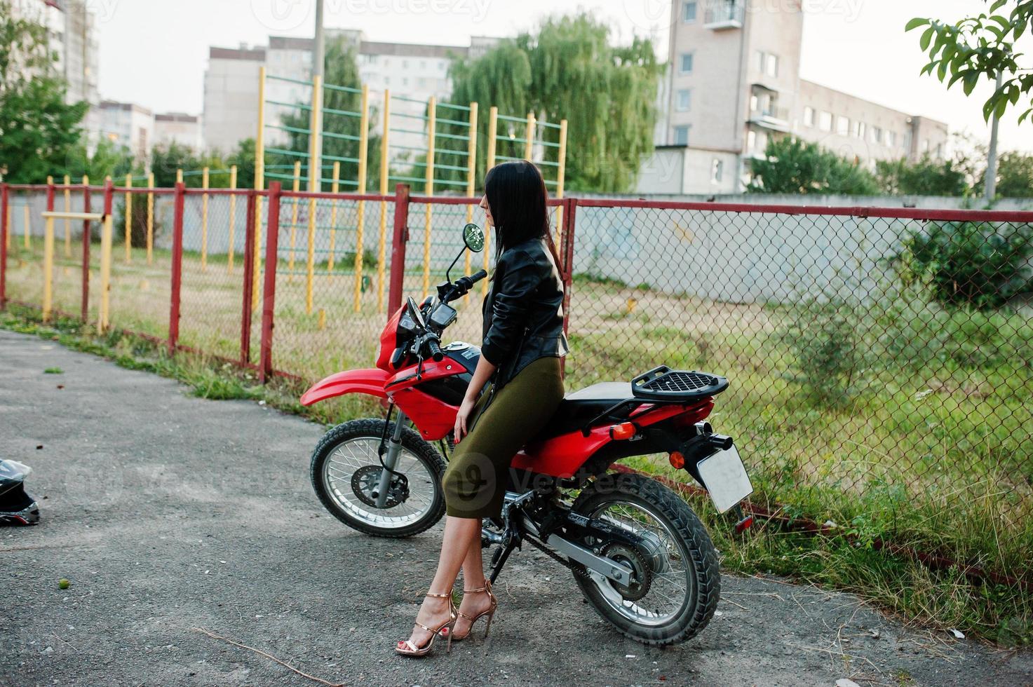 retrato de una mujer genial e impresionante con vestido y chaqueta de cuero negro sentada en una moto roja genial. foto