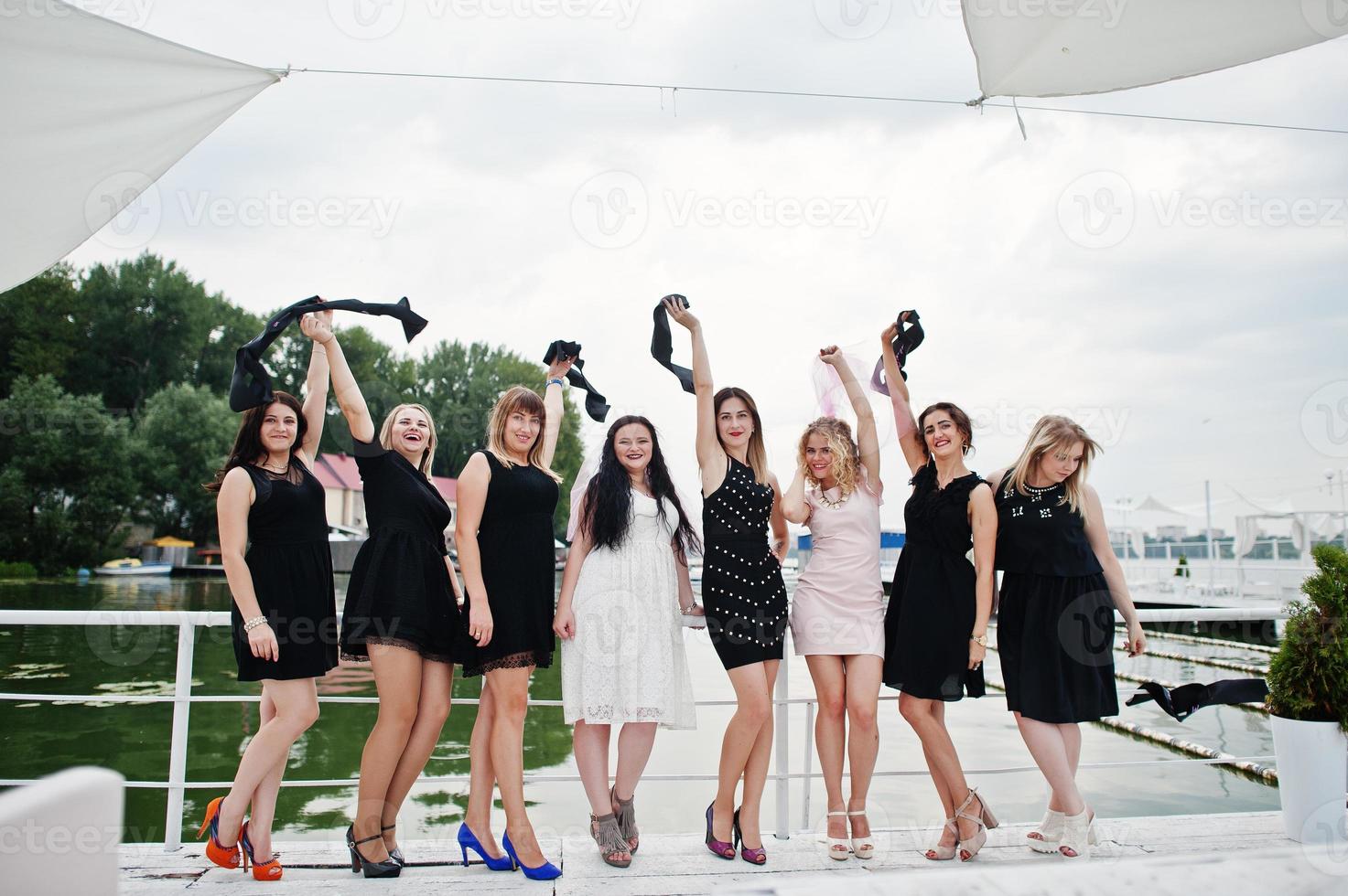 Group of 8 girls wear on black and 2 brides at hen party having fun at pier on beach side. photo