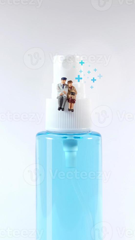 Elderly couple figure sitting on a  alcohol spray bottle. Covid-19 concept. photo
