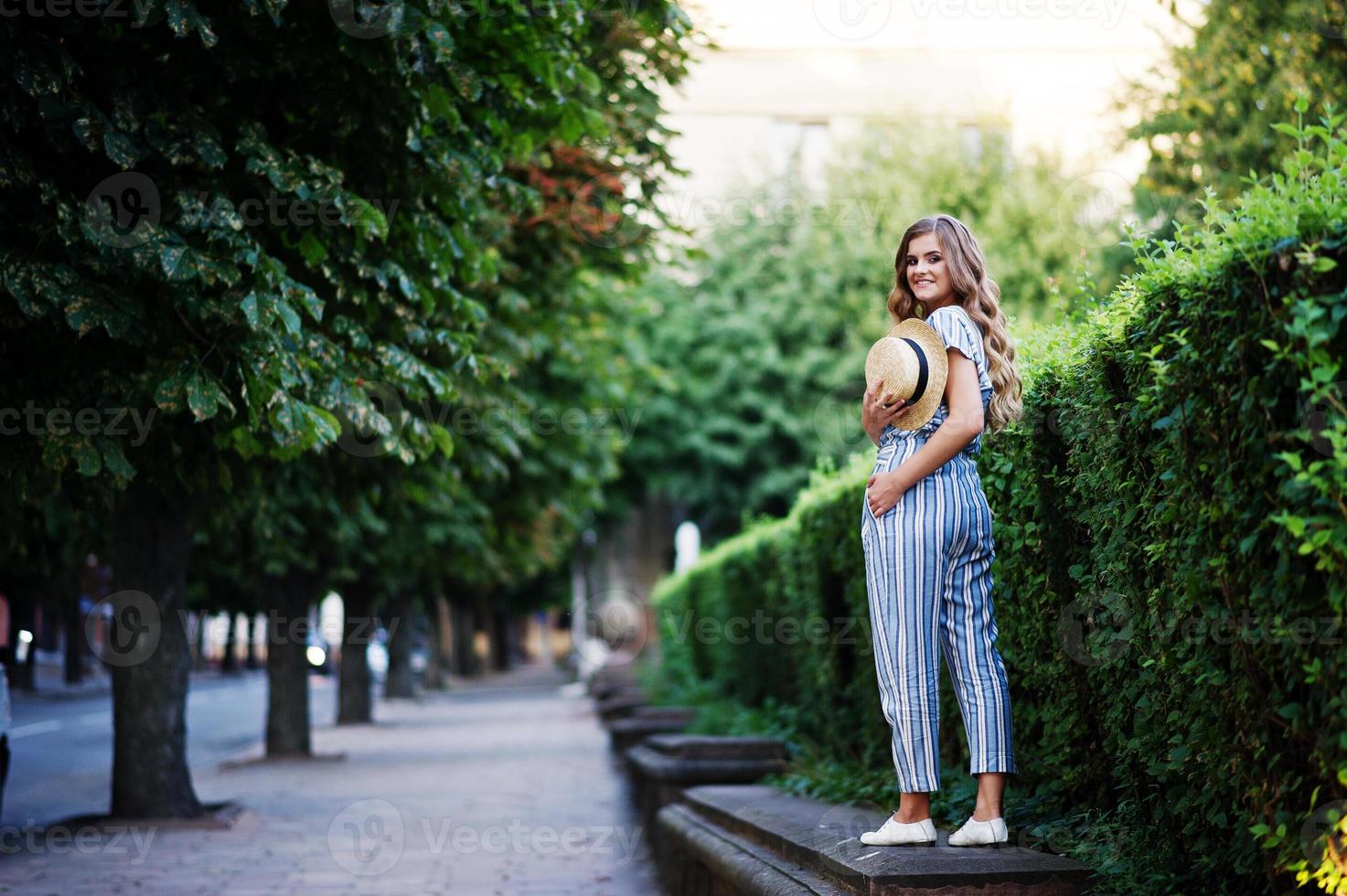 Portrait of a fabulous young woman in striped overall walking on the barrier in the park. photo