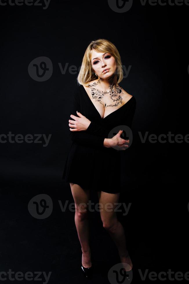 Studio portrait of blonde girl with originally make up on neck, wear on black dress at dark background. photo