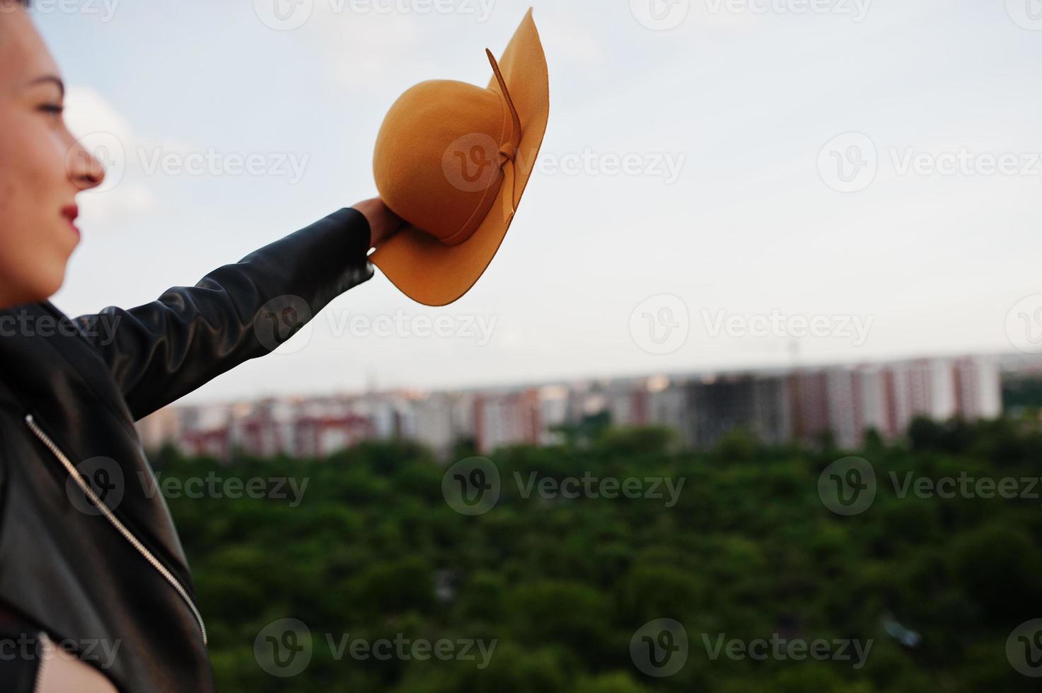 Portrait of an attractive woman waving her orange hat on top of the building in city. photo