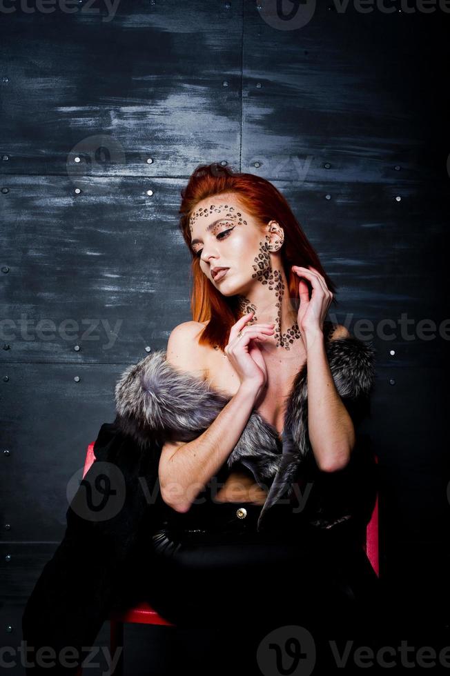 Fashion model red haired girl with originally make up like leopard predator against steel wall. Studio portrait on ladder. photo