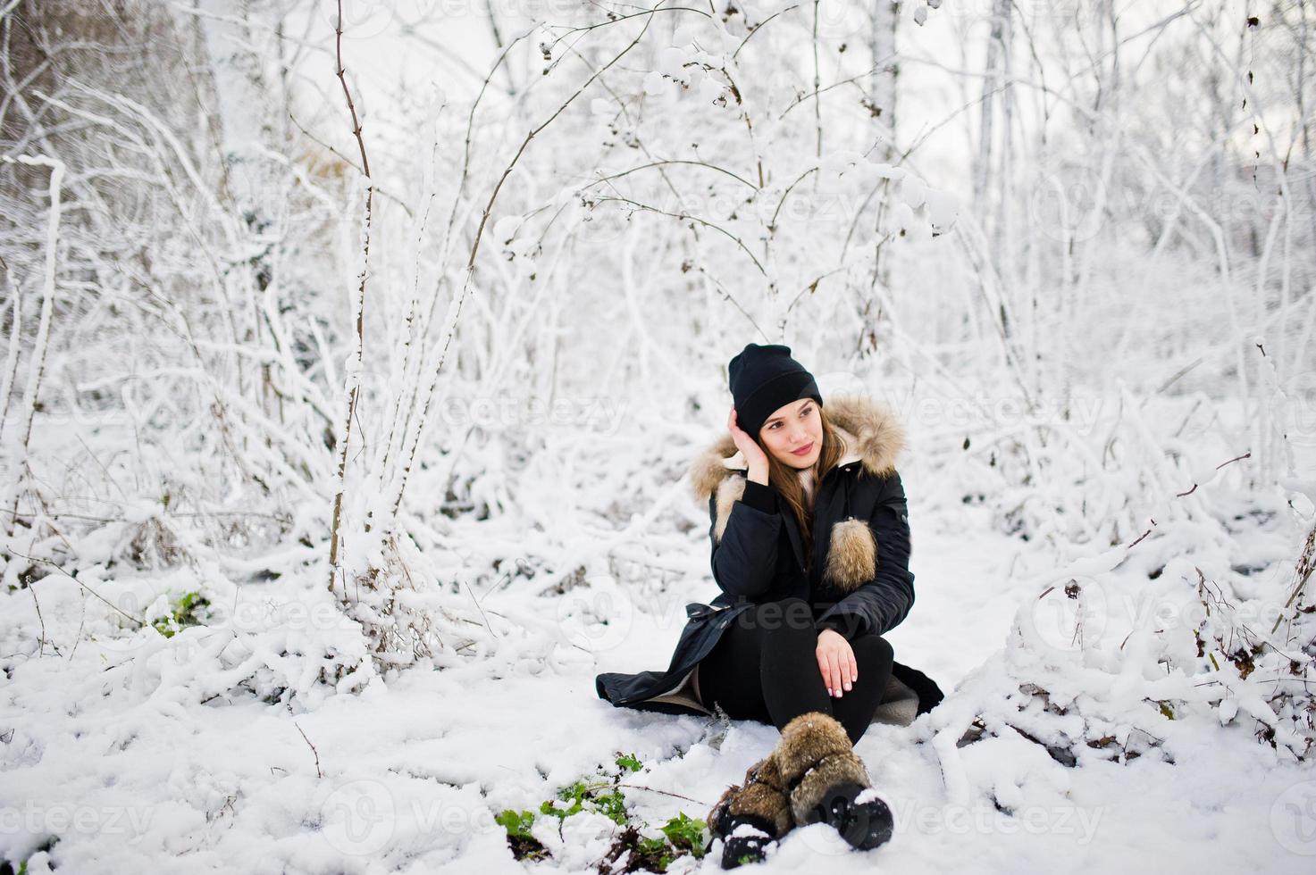 Beautiful brunette girl in winter warm clothing. Model on winter jacket and black hat. photo