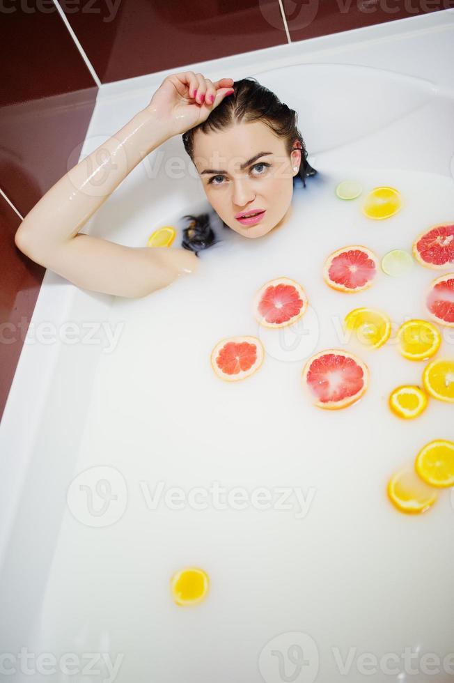 chica morena sexy en el baño con leche y frutas. baño de juventud para el cuerpo. foto