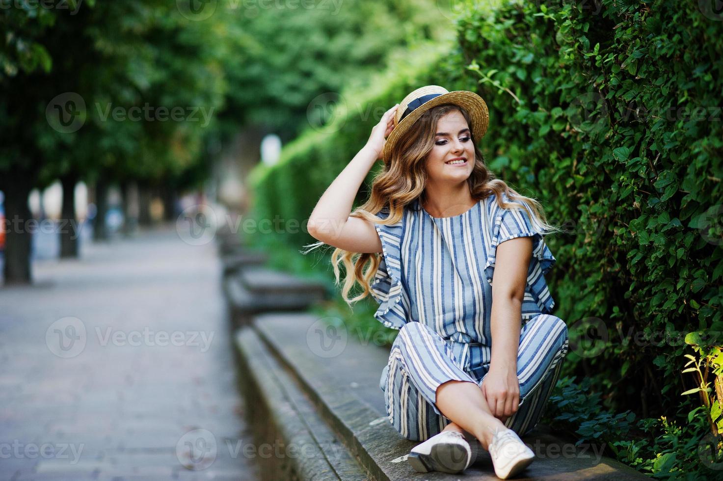 Portrait of a stunning young woman in striped overall sitting in the park. photo