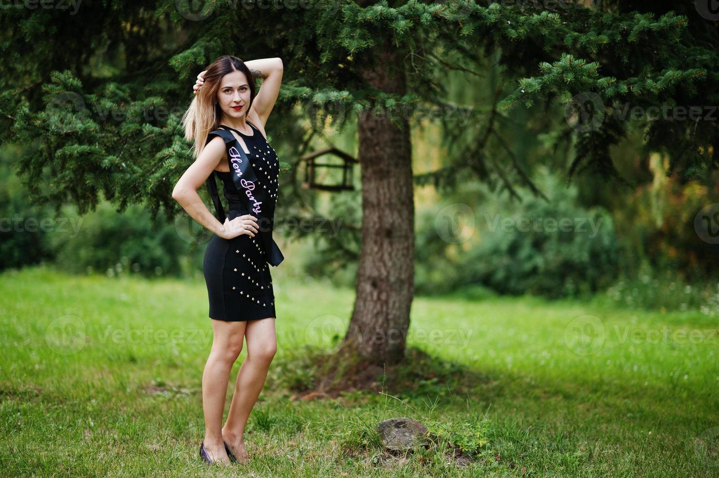retrato de una hermosa chica vestida de negro en una despedida de soltera, posada en el parque. foto