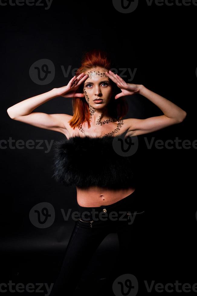 Fashion model red haired girl with originally make up like leopard predator isolated on black. Studio portrait. photo