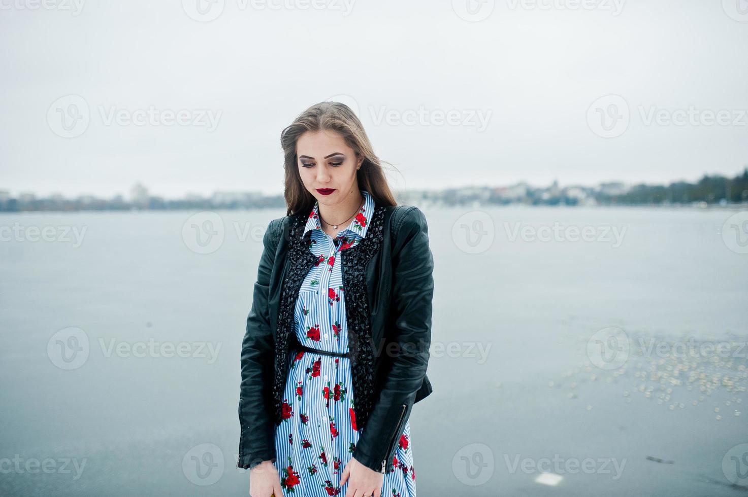 Stylish girl in leather jacket at winter day against frozen lake. photo