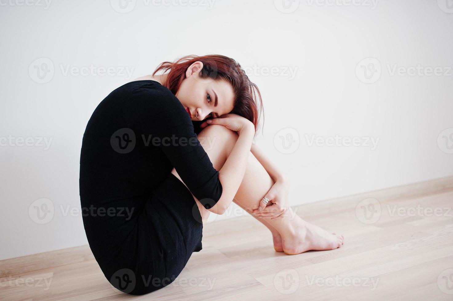 Red haired girl on black dress tunic against white wall at empty room. photo