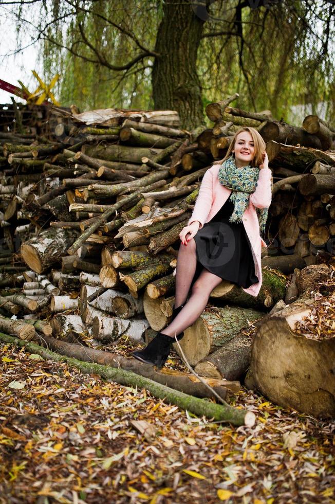 Young blonde girl at pink coat posed against wooden stumps background. photo