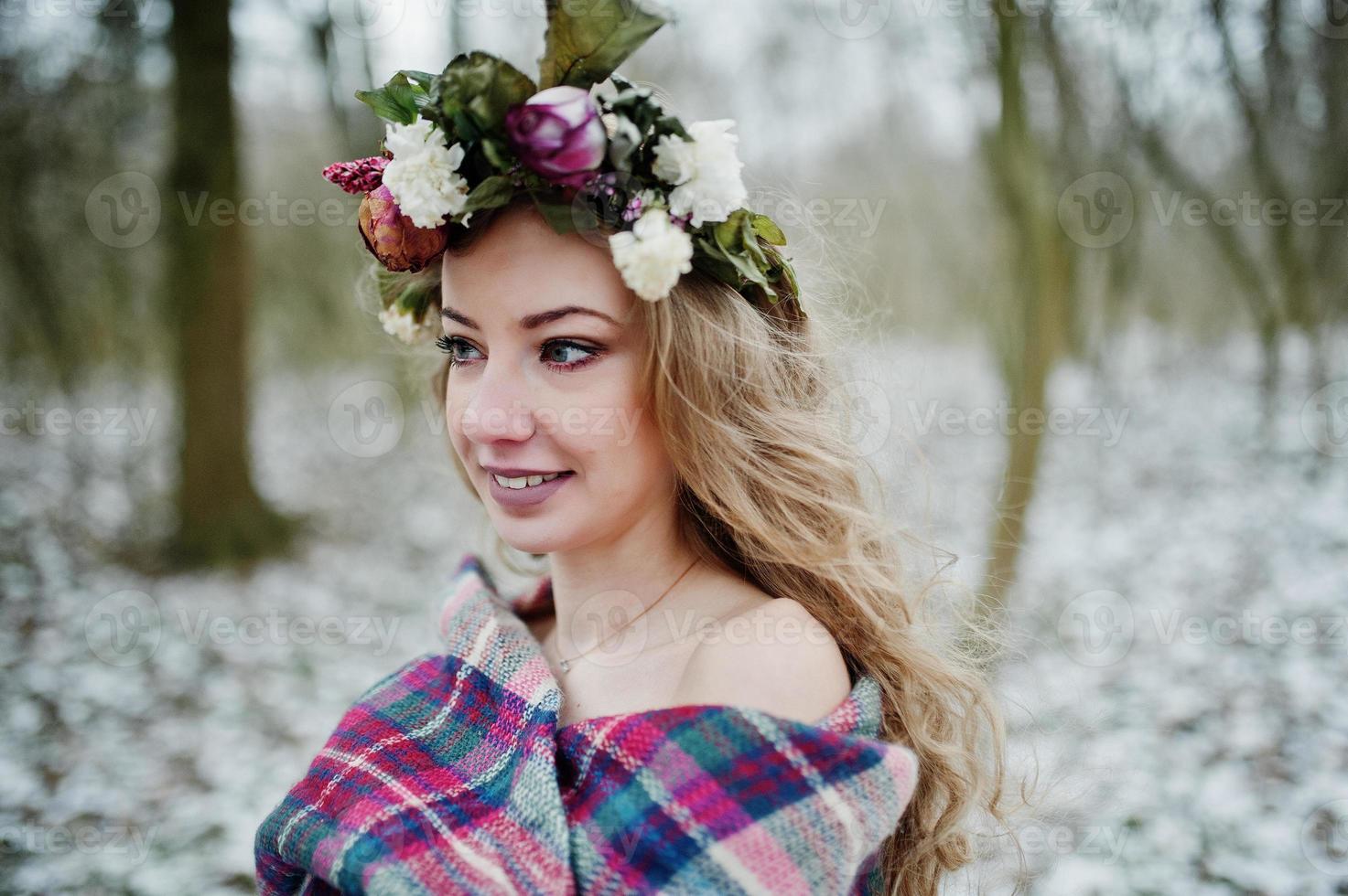 Curly cute blonde girl with wreath in checkered plaid at snowy forest in winter day. photo