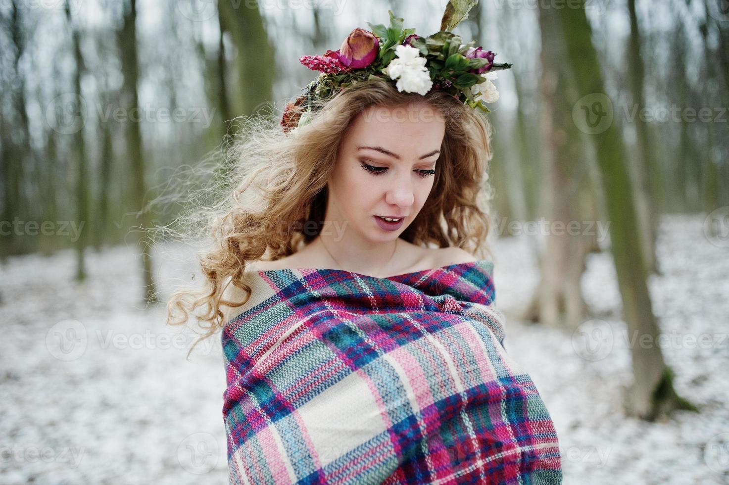 Curly cute blonde girl with wreath in checkered plaid at snowy forest in winter day. photo
