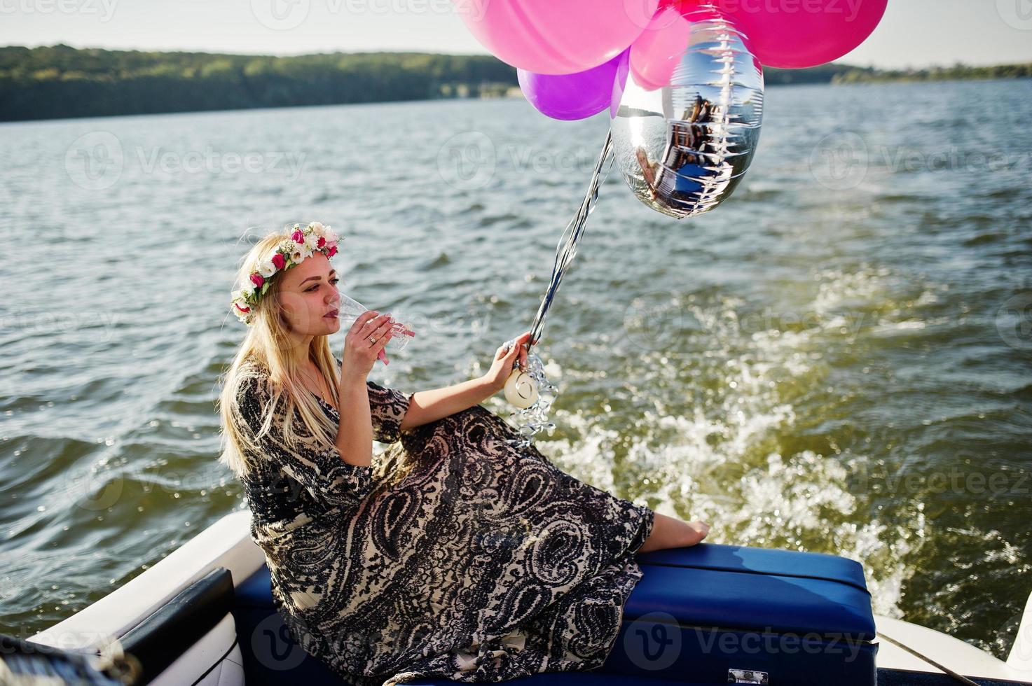 Blonde girl in wreath sitting on yacht at hen party with champagne. photo
