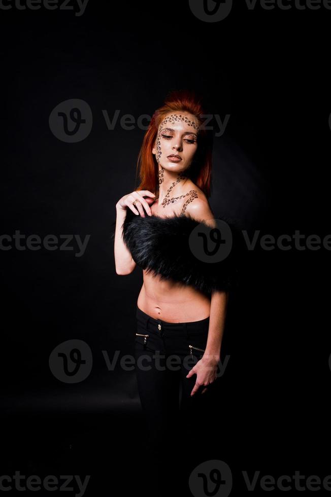 Fashion model red haired girl with originally make up like leopard predator isolated on black. Studio portrait. photo