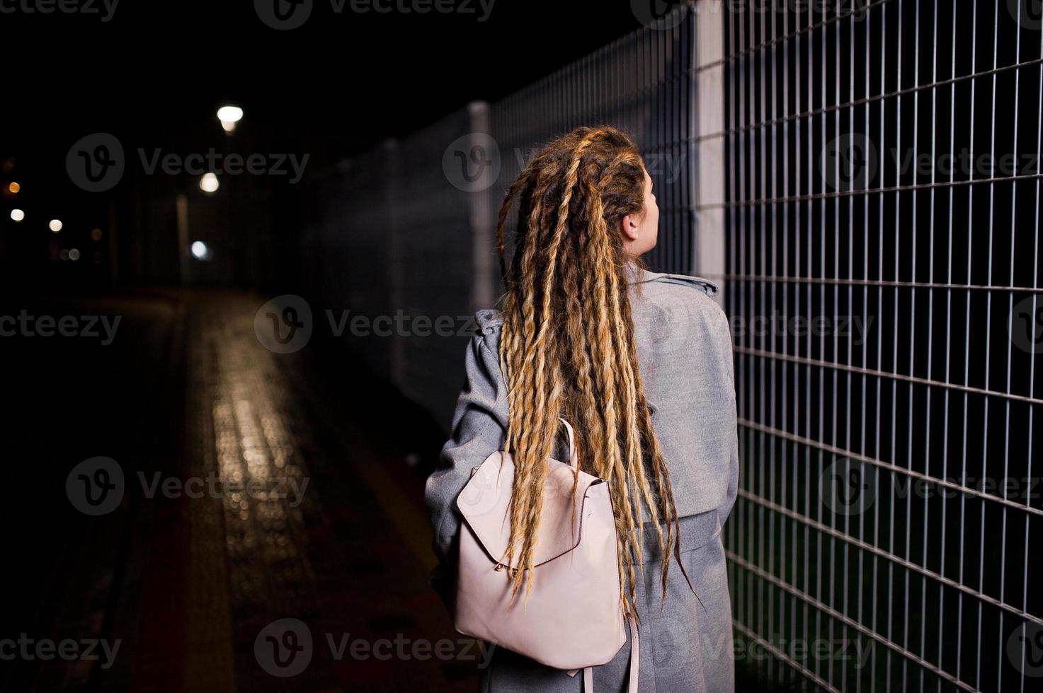 Girl with dreadlocks walking at night street of city. photo