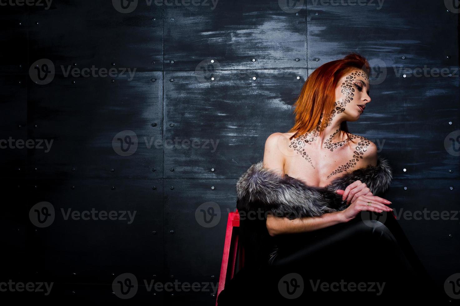 Fashion model red haired girl with originally make up like leopard predator against steel wall. Studio portrait on ladder. photo