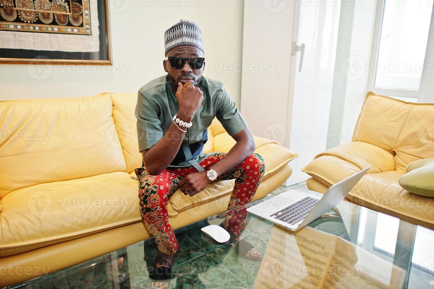 Rich african man sitting on sofa at his appartment and working on notebook. photo