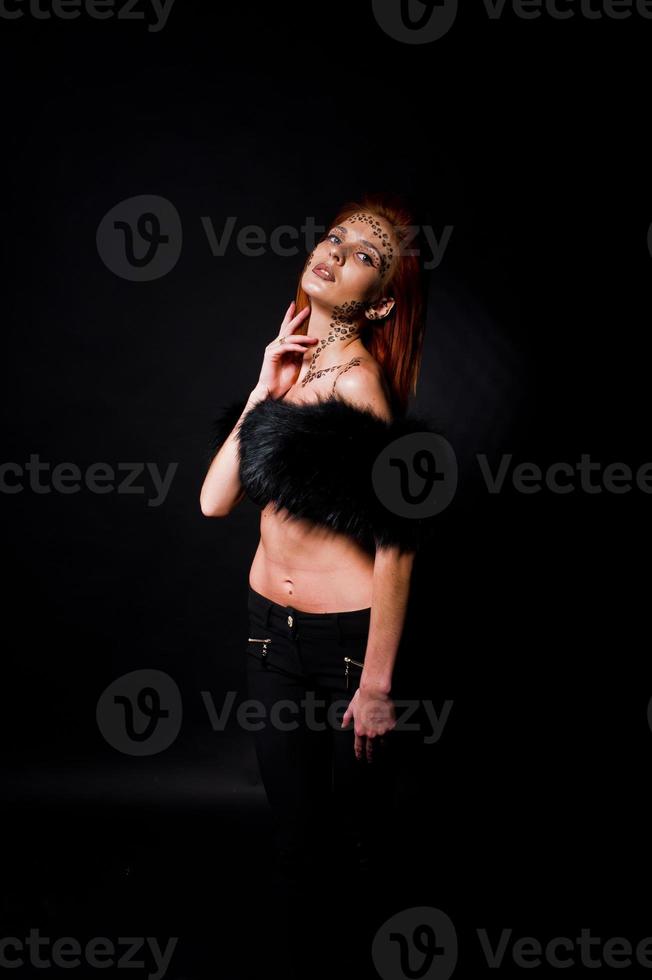 Fashion model red haired girl with originally make up like leopard predator isolated on black. Studio portrait. photo