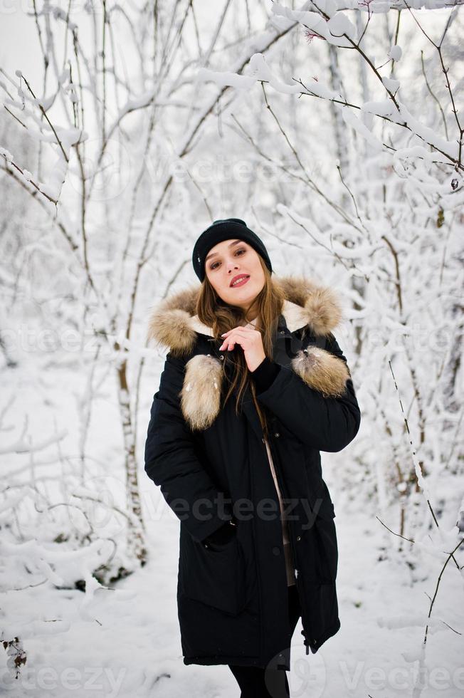 Beautiful brunette girl in winter warm clothing. Model on winter jacket and black hat. photo