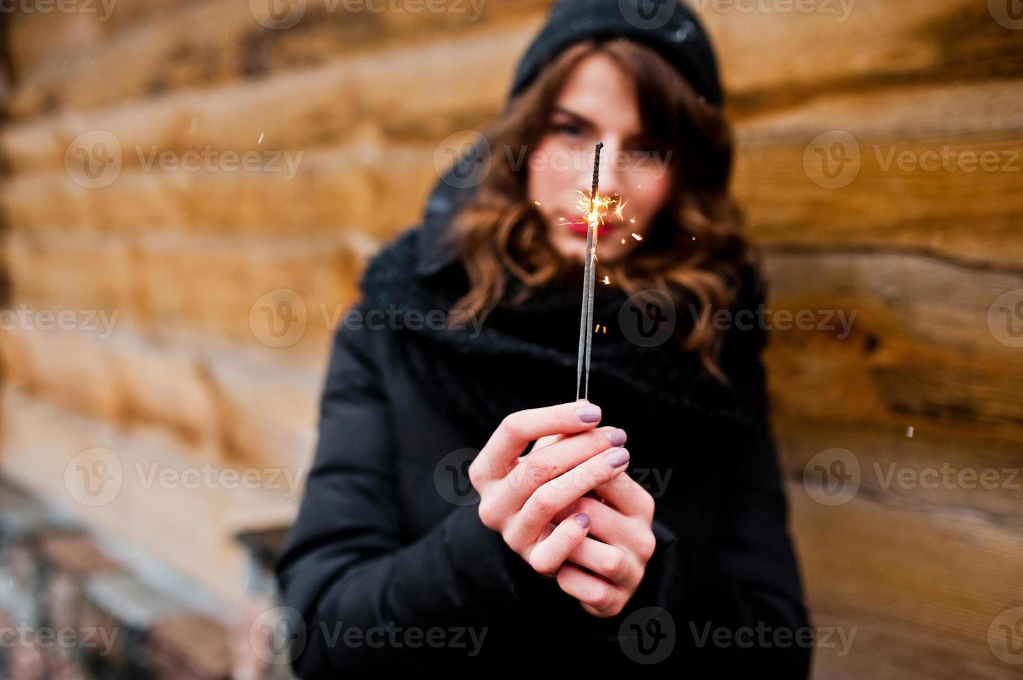 Portrait of brunette curly girl in black jacket, hat and scarf with bengal lights in hand. photo