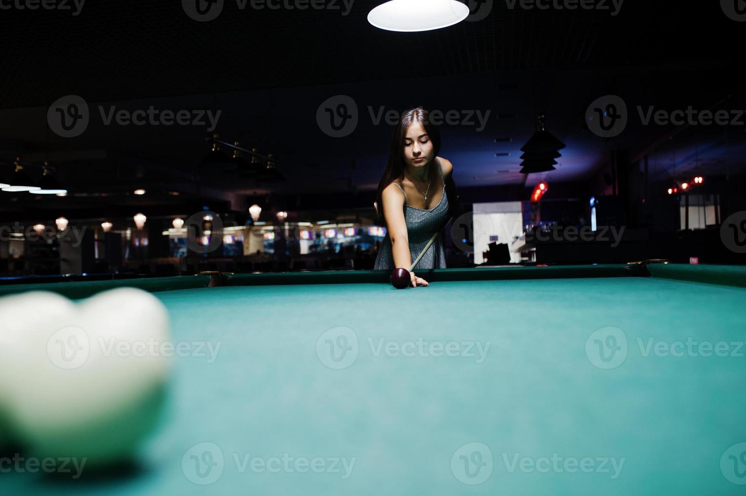 Portrait of an attractive young woman in dress playing pool. photo