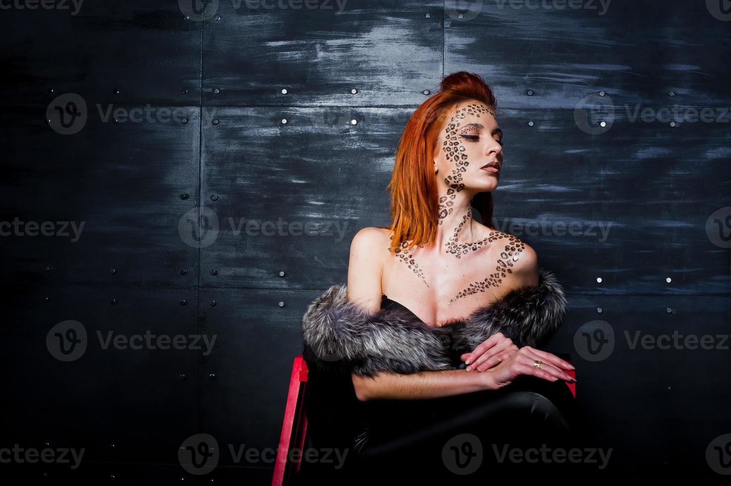 Fashion model red haired girl with originally make up like leopard predator against steel wall. Studio portrait on ladder. photo