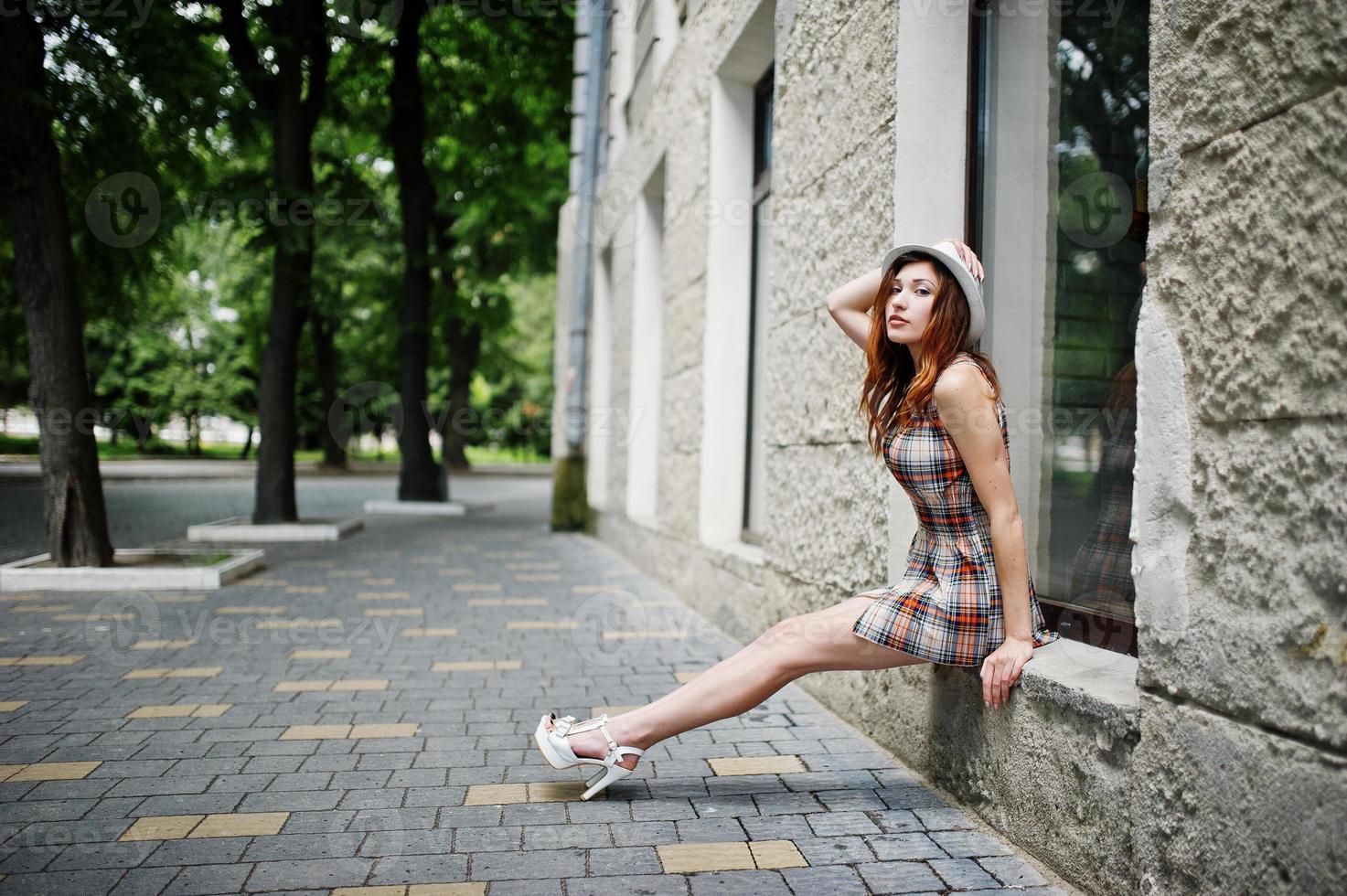 Amazing long legs with hig heels girl wear on hat sitting on the window sill on streets of city. photo